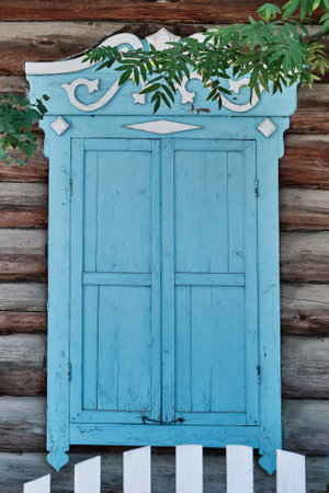 Old wooden window with closed worn blue shutters. Carved architraves, log facade of a typical rural wooden house, Buryatia, Russia. architecture conceptの写真素材