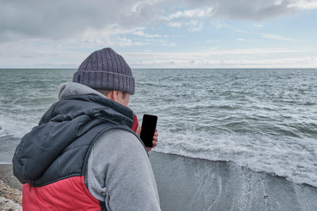 Over shoulder view of senior man using cellphone with black empty screen for mockup, outdoors near...