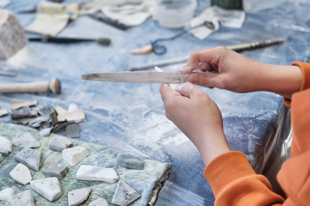 Hands of child processing ornamental stone with file at stone carving masterclass. Making amulets, pendants. Project of children's creativity, crafts. handmade concept.の写真素材