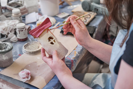 Hands of girl painting with brush toy fantasy house made of plaster at masterclass. Project of children's creativity, crafts. handmade concept.の写真素材