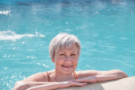 Close-up portrait of senior woman in outdoor thermal swimming pool. Elderly caucasian woman with gray short hair in swimsuit smiling and looking at camera. Active elderly concept. copy spaceの写真素材