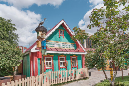 Kazan, Russia - June 8, 2023: Colorful rural house in Tatar style in national tourist and entertainment complex Tugun Avylym. Decorative birdhouses and sculpture of stork in nest. travel conceptのeditorial素材