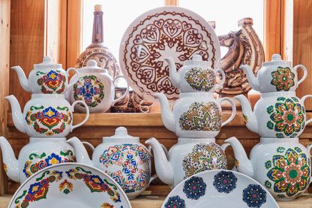 Kazan, Russia - June 8, 2023: Ceramic teapots and plates with colorful traditional Tatar floral ornament on wooden shelves in a souvenir shop. travel conceptのeditorial素材