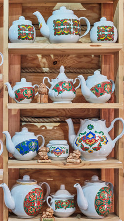 Kazan, Russia - June 8, 2023: Ceramic teapots and sugar bowls with colorful traditional Tatar floral ornament on wooden shelves in a souvenir shop. travel conceptのeditorial素材
