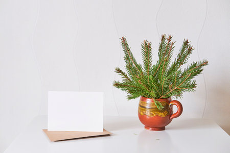Blank paper on craft envelope, bouquet of christmas tree branches in handmade clay mug.の写真素材
