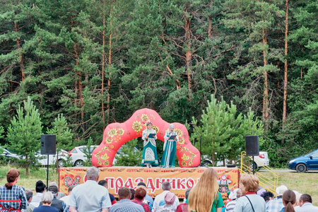 Aromashevo, Russia - June 15, 2023: Concert on rural holiday, day of the small motherland. Concert hosts, two women, Asian and Caucasian, in stylized Tatar and Russian clothes, on stage.のeditorial素材