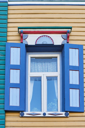 Traditional window with carved wooden colorful architraves and exterior wooden shutters. Facade of historical merchant house 19th century, Kazan, Russia. Architecture concept.の写真素材