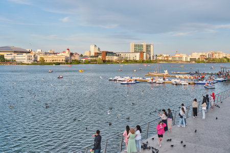 Kazan, Russia - June 17, 2023: People relaxing on Nizhny Kaban lake in downtown, walking along embankment, riding pedalos. Active leisure. Summer city landscape.のeditorial素材