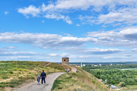 Yelabuga, Russia - June 18, 2023: Dad and son walking along path to white stone tower, fortress-mosque of 12th century. Devil's hillfort, ruins of ancient settlement, historical monument.のeditorial素材