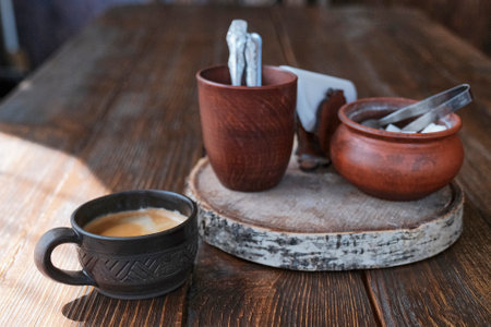 Brown handmade clay cup with black coffee. Wooden table. Clay crockery, cutlery glass, sugar bowl,...