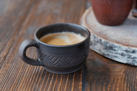 Brown handmade clay cup with black coffee. Wooden table. Clay crockery. Rustic coffee serving, natural materials. Selective focus. Close-up. Copy spaceの写真素材