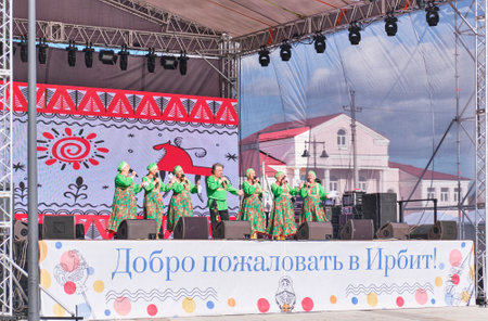 Irbit, Russia - August 11, 2023: Vocal group of senior people in Russian style concert outfits performing on decorated stage, singing into microphones. Traditional summer Irbit fair.のeditorial素材