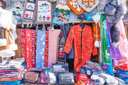 Souvenir shop at local market, Almaty, Kazakhstan. Silk stoles with traditional embroidery, bright robe in Kazakh style, elegant national vest, fur hat, felt paintings, leather bags with pattern.の写真素材