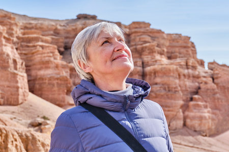 Closeup portrait of senior Caucasian woman with gray hair looking up over background of rocks of Charyn Canyon. National natural park in Kazakhstan. Natural landmarks near Almaty. Travel concept.の写真素材