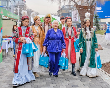 Almaty, Kazakhstan - March 20, 2024: Group of womens and mens in traditional national Kazakh clothes walking down pedestrian street at crafts fair on eve of spring festival Nowruz.Close-upのeditorial素材