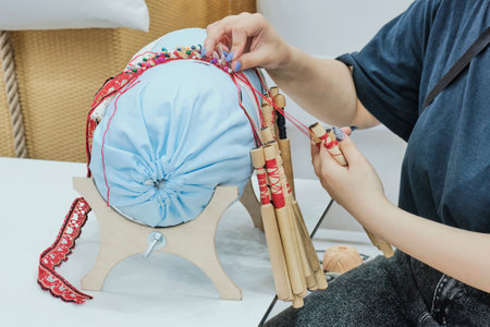Girl's hands spin braid on bobbins. Special lace weaving technique, pattern created using special tools: roller and bobbins. Bobbins are special wooden sticks on which weaving threads are wound.の写真素材