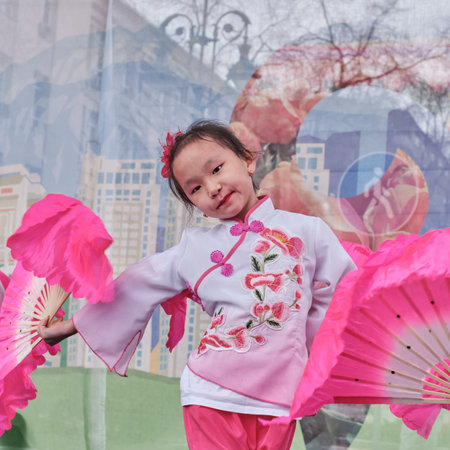 Almaty, Kazakhstan - March 21, 2024: Cute little Asian girl dancing Chinese fan dance during celebration of spring holiday of Nowruz.のeditorial素材