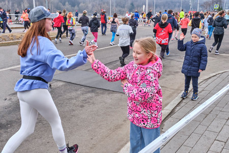 April 7, 2024 - Moscow, Russia: Traditional April five kilometer race in Luzhniki stadium area. Little spectator girl greets young woman amateur runner by clapping her palm against athlete s palm.のeditorial素材