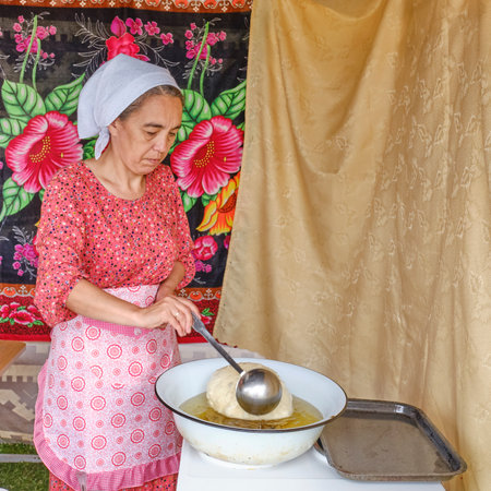 Tobolsk, Russia - July 20, 2024: Cookery masterclass on baking baursaks, fluffy pieces of dough, deep fried. Asian female chef holds ladle in his hand. Tatar gastronomic festival Siberian baursakのeditorial素材