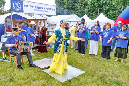Tobolsk, Russia - July 20, 2024: Happy smiling senior Asian woman in national Tatar costume dances to accompaniment of accordion at Tatar Gastronomic Festival to applause of audienceのeditorial素材
