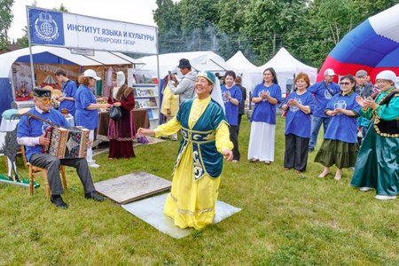 Tobolsk, Russia - July 20, 2024: Audience applause dancing smiling senior Asian woman in national Tatar costume and skullcap to accompaniment of accordion at Tatar Gastronomic Festival.のeditorial素材