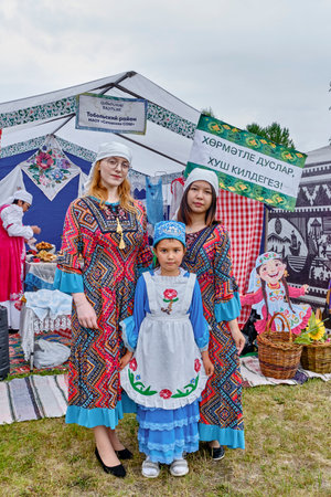Tobolsk, Russia - July 20, 2024: Young woman and two girls, guests of traditional Tatar gastronomic festival Siberian baursak, in festive national clothes pose near decorated tentのeditorial素材