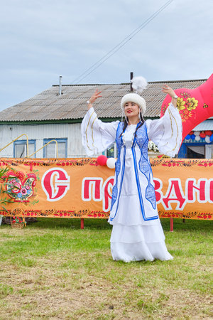 Tyumen, Russia - July 6, 2024: Young Asian girl in national costume performing Bashkir dance on grass in front of rural club at festival Village Day.のeditorial素材
