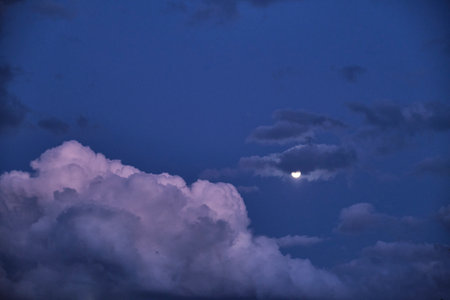 Night dark blue sky with fluffy clouds and round moon as fairy tale background. Evening cloudy...