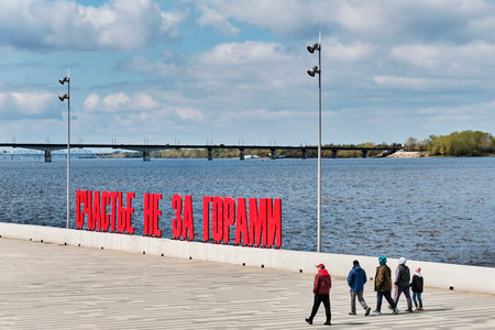 Perm, Russia - May 18, 2024: Group of people walking past large voluminous red Russian letters on Kama River embankment. Text -Happiness Is Not Far Away. Art object, symbol of city of Perm.のeditorial素材