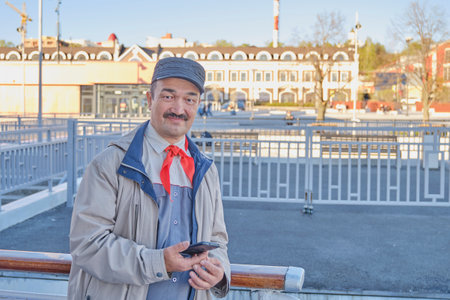 Street portrait of senior Asian smiling happy man in red pioneer tie, former member of children's pioneer organization in Soviet Union. Looking at camera, modern mobile phone in his hand.の写真素材