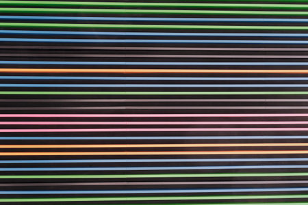 Textured wall with horizontal stripes in vibrant colors alternating against dark background. Lines maintain uniform spacing, creating modern, visually striking pattern. Colorful striped wallの写真素材