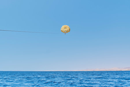 Senior white woman with gray hair under yellow dome of parachute enjoying parasailing against blue sky, Red Sea and egyptian coast. Extreme entertainment. Copy spaceの写真素材