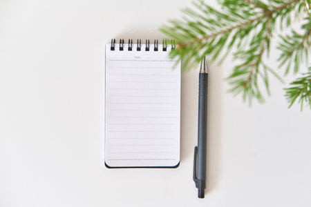 Blank spiral notebook and black pen on white surface, with green fir tree branches in top right corner. Minimalist composition with seasonal touch. Top viewの写真素材