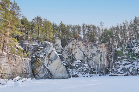 Scenic winter view of Talc Stone lake, surrounded by vertical rock cliffs and pine forest. Snow-covered terrain and frozen lake in Bazhov Nature Park, Russia.の写真素材