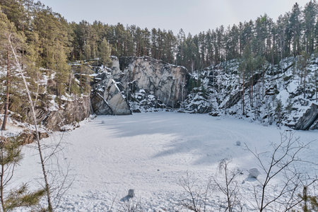 Frozen lake in talc quarry surrounded by snowy pine forest in winter. Scenic natural landscape in Bazhov nature Park, Sverdlovsk Region, Russia.の写真素材