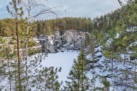 Snow-covered Talc Stone or Talkov Kamen lake surrounded by pine forest and rocky cliffs in Bazhov Nature Park, Ural, Russia, captured in winter.の写真素材