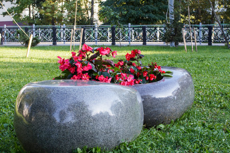 Japanese-inspired flower bed with vibrant pink begonias and seating arrangement in urban park. Minimalist design with smooth granite stone. Urban landscaping, Zen aesthetics, outdoor relaxation.の写真素材