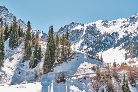 Shymbulak ski resort, Almaty, Kazakhstan. Kerey-Zhanibek Khandar street on a spring sunny day. Natural landscape with a road up the mountain, rocky slopes covered with snow and trees.の写真素材