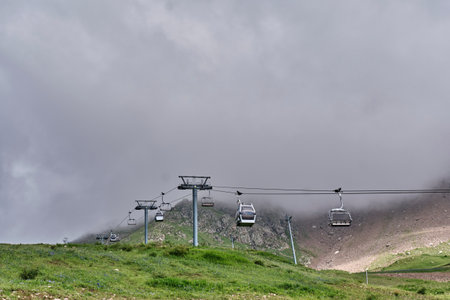 Ski lifts of the Kombi 2 cable car line ascending a green mountain slope in summer, surrounded by...