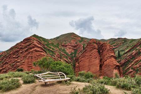 A bench made of wooden sticks on a viewing platform against the backdrop of amazing red clay and sand cliffs. Jety-Oguz Gorge, Kyrgyzstanの写真素材