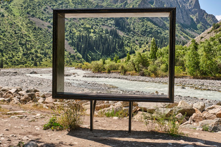 Outdoor photo zone with large empty frame overlooking mountain river, green hills, and conifer forest in Ala-Archa National Park, Kyrgyzstan, on a sunny summer day.の写真素材