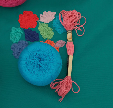 Close-up of yarn ball, embroidery threads, and handmade chain stitch floral motifs on green fabric. Materials and tools for traditional needlework and textile art.の写真素材