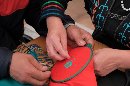 Close-up of hands during a tambour embroidery workshop, stitching a traditional pattern on red fabric in an embroidery hoop.の写真素材