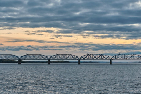 Panoramic view of Syzran or Alexander Bridge spanning a wide Volga river at sunset. Industrial architecture and transportation infrastructure against scenic evening sky. Samara region, Russiaの写真素材