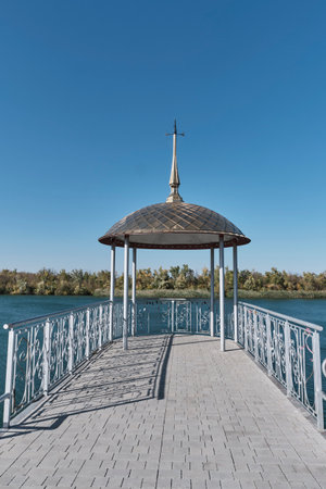 Elegant riverside gazebo with metal spire roof and ornate railing over water on clear sunny day. Tranquility and architectural beauty. Don River embankment, Romanovskaya village, Russiaの写真素材