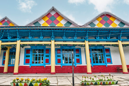 Vibrant, wooden Dungan Mosque in Karakol, Kyrgyzstan, known for its Chinese pagoda architecture and nail-free construction. Bright blue windows, yellow columns, and colorful patterned roof.