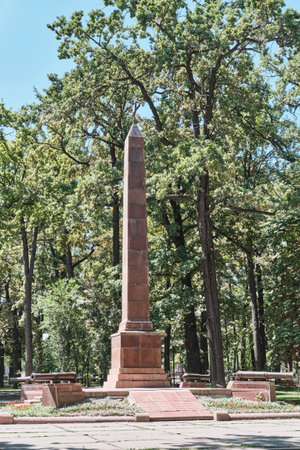 Kyrgyzstan, Bishkek - July 12, 2025: Towering stone obelisk flanked by cannons. Memorial to Red Guards stands over mass grave of Bolshevik fighters who fell in 1918. Located in Dubovy ,Oak, parkの写真素材