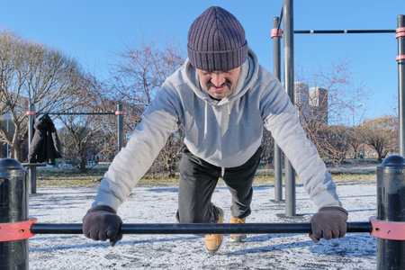 Mature man is intensely focused on performing push-up on parallel bars at outdoor calisthenics gym....