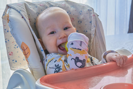 Close-up portrait of a cheerful infant with a wide smile, sitting comfortably in a high chair. Baby...
