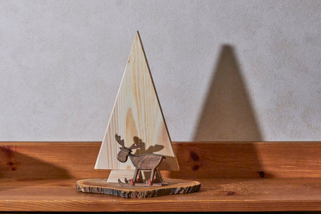 Simple yet stylish wooden Christmas tree and carved reindeer figure on log slice base. Minimalist holiday decoration on wooden shelf, casting pronounced shadow.の写真素材